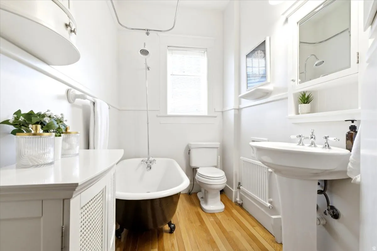 Pedestal sink with chrome fixtures, clawfoot tub with shower attachment, and wood-finish flooring