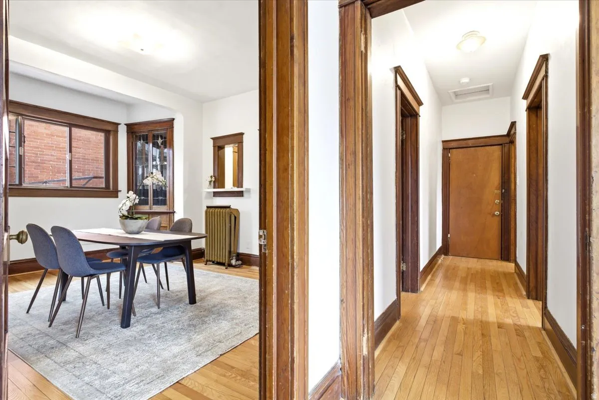Hardwood flooring extends throughout the hallway and into a room featuring a bay window, wood trim, and a built-in corner cabinet with leaded glass