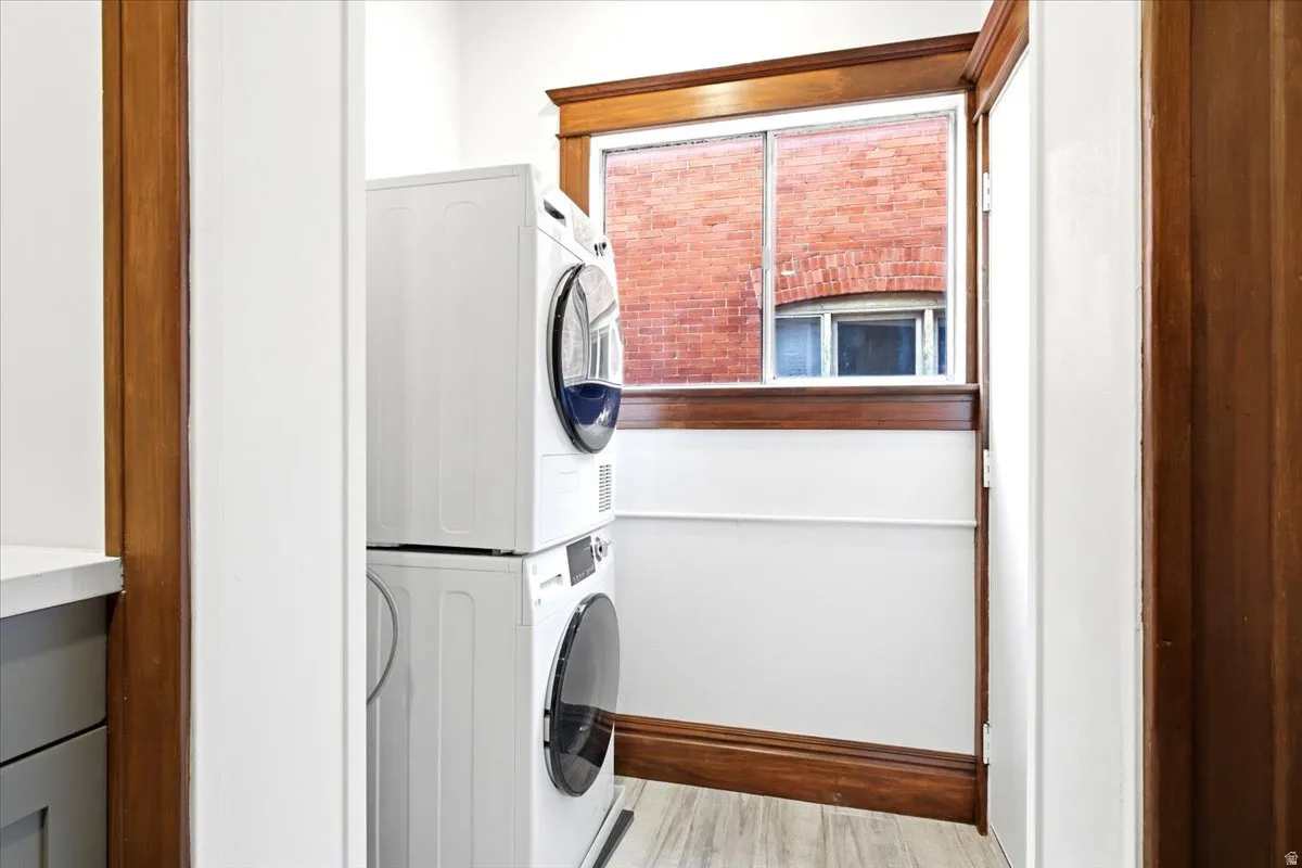 Dedicated laundry area with stackable appliances, wood-finish trim, and light wood-look flooring