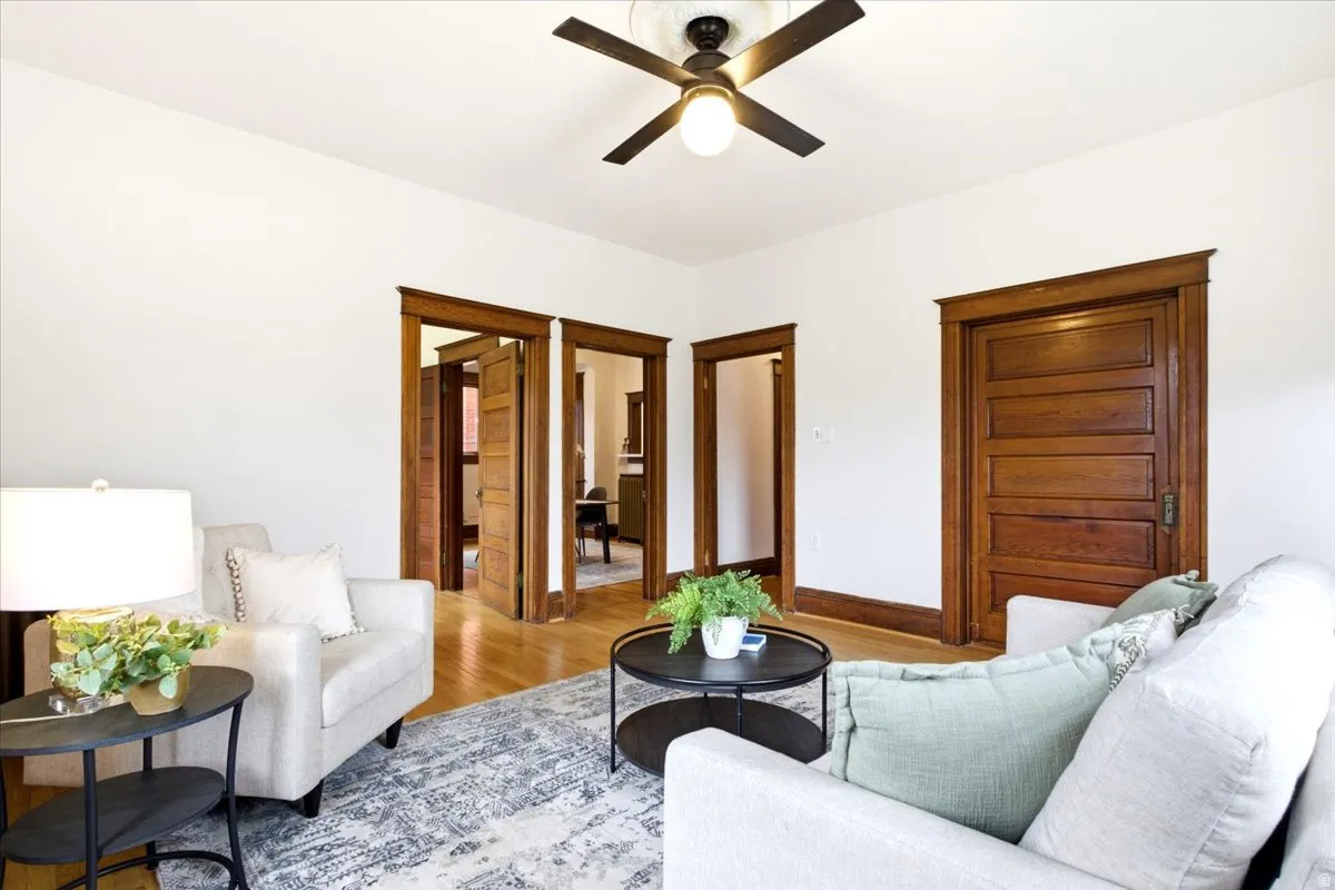 Living space featuring a ceiling fan, wood-finish flooring, and multiple doorways with natural wood trim