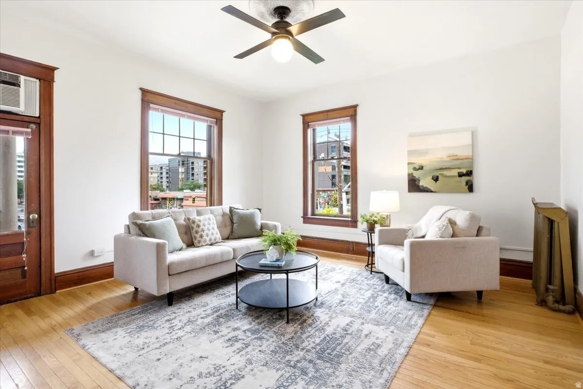 Bright living area featuring wood-finish flooring, two large windows with dark wood trim, and a ceiling fan with light fixture