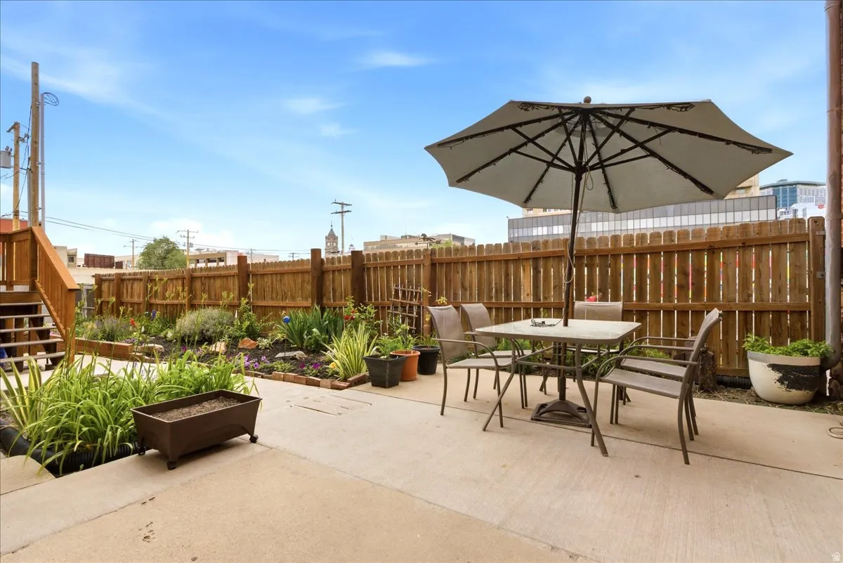 Patio area featuring concrete surfacing, a wooden privacy fence, raised garden beds with established plantings, and a wooden exterior staircase