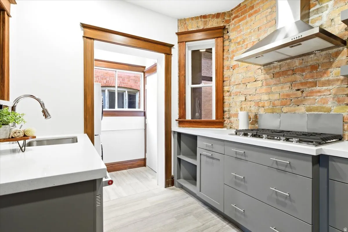 Modern kitchen featuring a stainless steel range hood, a gas cooktop, and light grey cabinetry with brushed nickel hardware