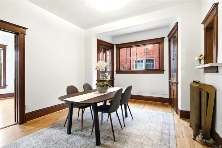 Dining area featuring hardwood flooring, white walls, dark wood trim, large windows with dark wood frames, and a built-in shelf