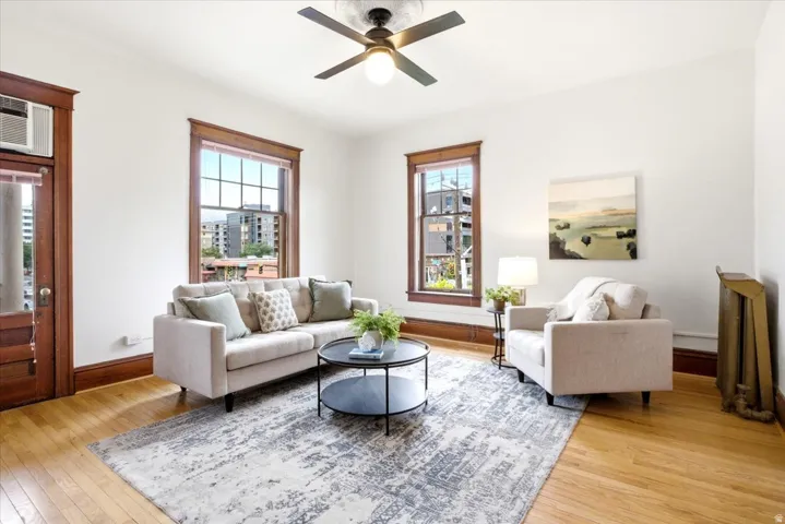 Bright living area featuring wood-finish flooring, two large windows with dark wood trim, and a ceiling fan with light fixture