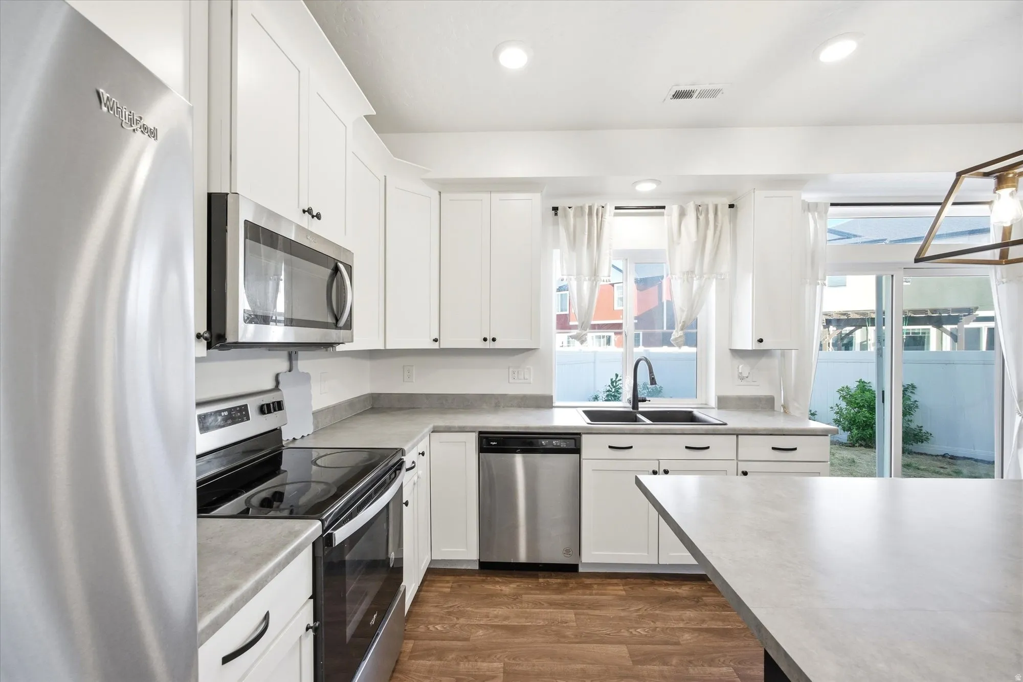Kitchen featuring white shaker cabinetry, stainless steel appliances, light-toned countertops, wood-finish flooring, and a sliding glass door to the exterior
