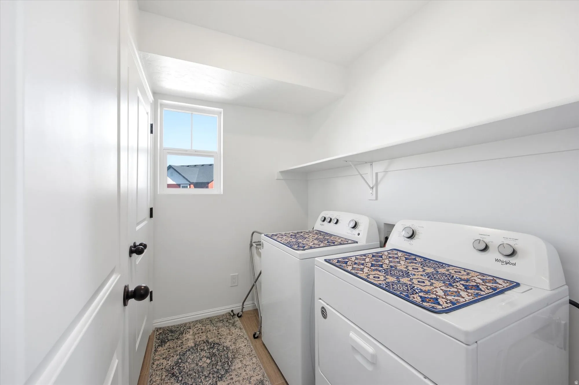 Bright laundry space featuring a window, built-in shelving, two doors with black hardware, and wood-finish flooring