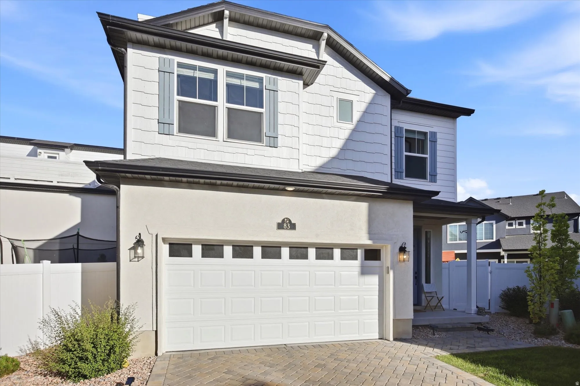Two-story residence featuring a white paneled and stucco exterior, a two-car garage with panel windows, a covered front porch, and a paved driveway