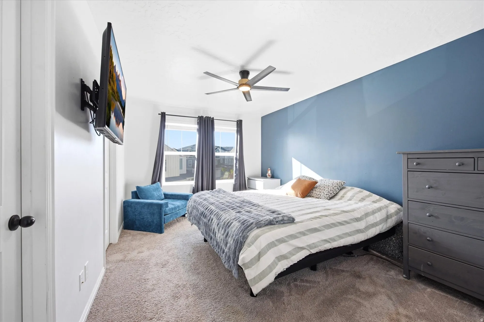 Bedroom featuring a full accent wall, plush carpeting, multiple windows with dark curtains, and a ceiling fan with integrated lighting