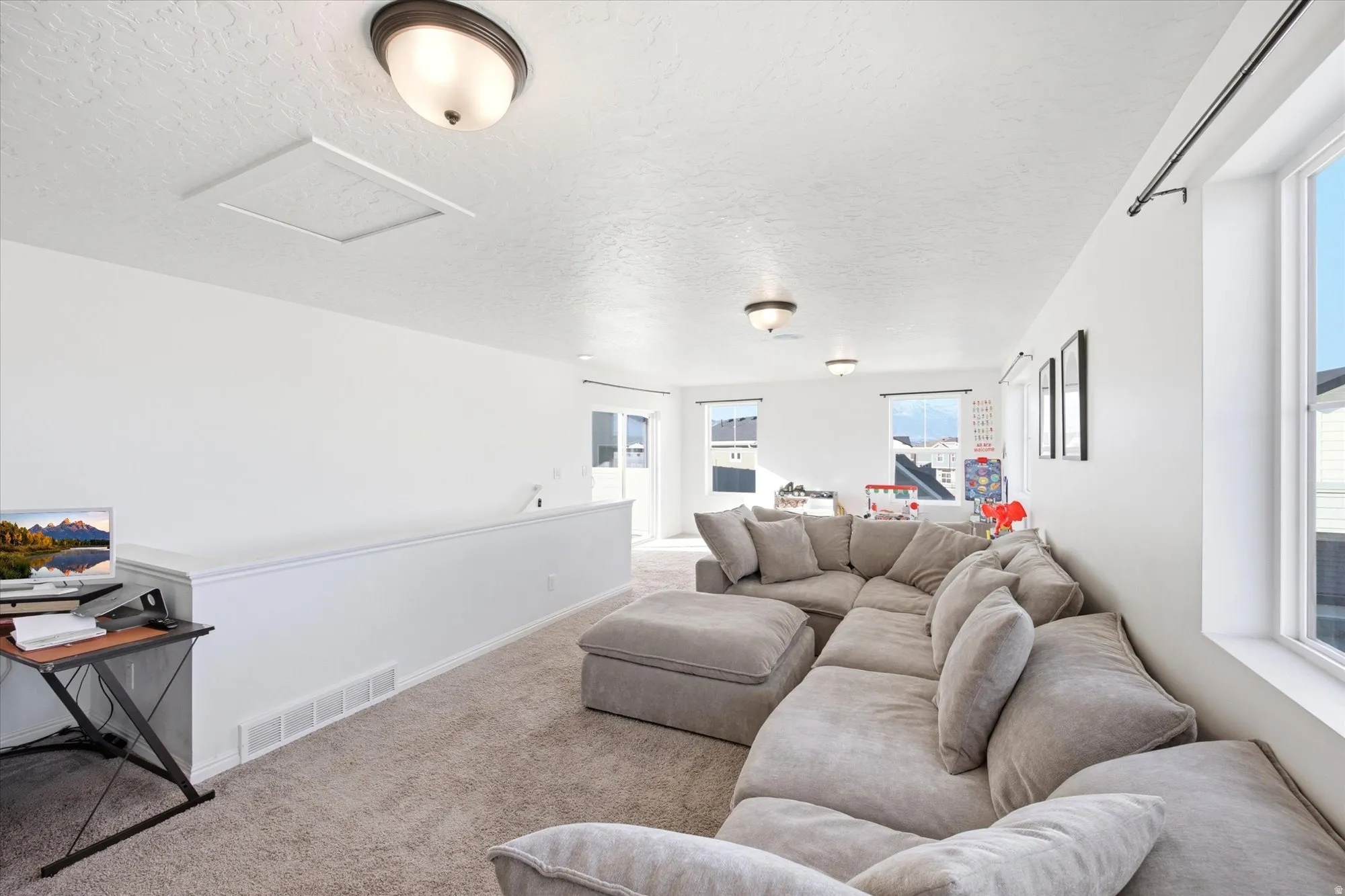 Spacious upper-level loft area with neutral-toned carpet flooring, bright white walls, multiple windows providing natural light, and recessed ceiling lighting