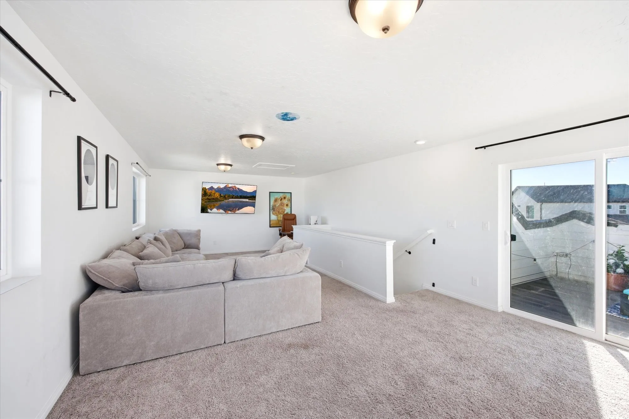 Spacious carpeted room featuring a white railing, multiple windows, a sliding glass door, and flush-mount ceiling lighting