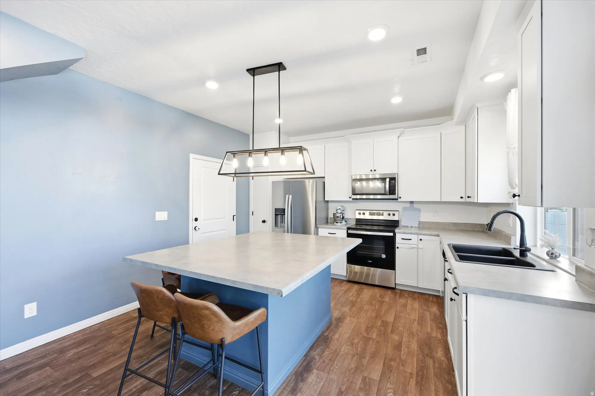 Kitchen featuring an island with seating, white cabinetry, integrated stainless steel appliances, and wood-finish flooring