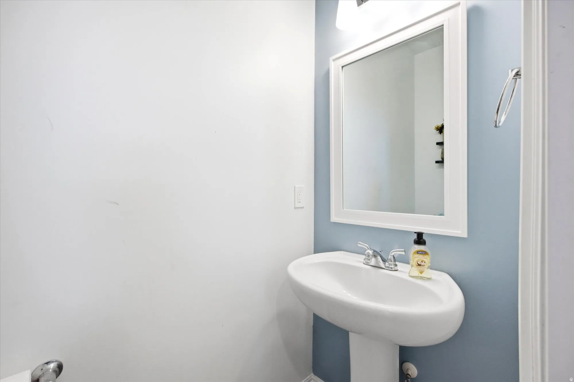 Pedestal sink with chrome faucet, complemented by a framed mirror and wall-mounted light fixture