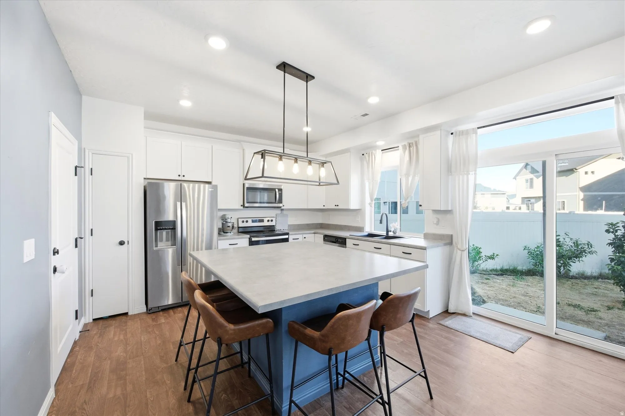 Modern kitchen featuring a central island with seating, white cabinetry, stainless steel appliances, and wood-finish flooring