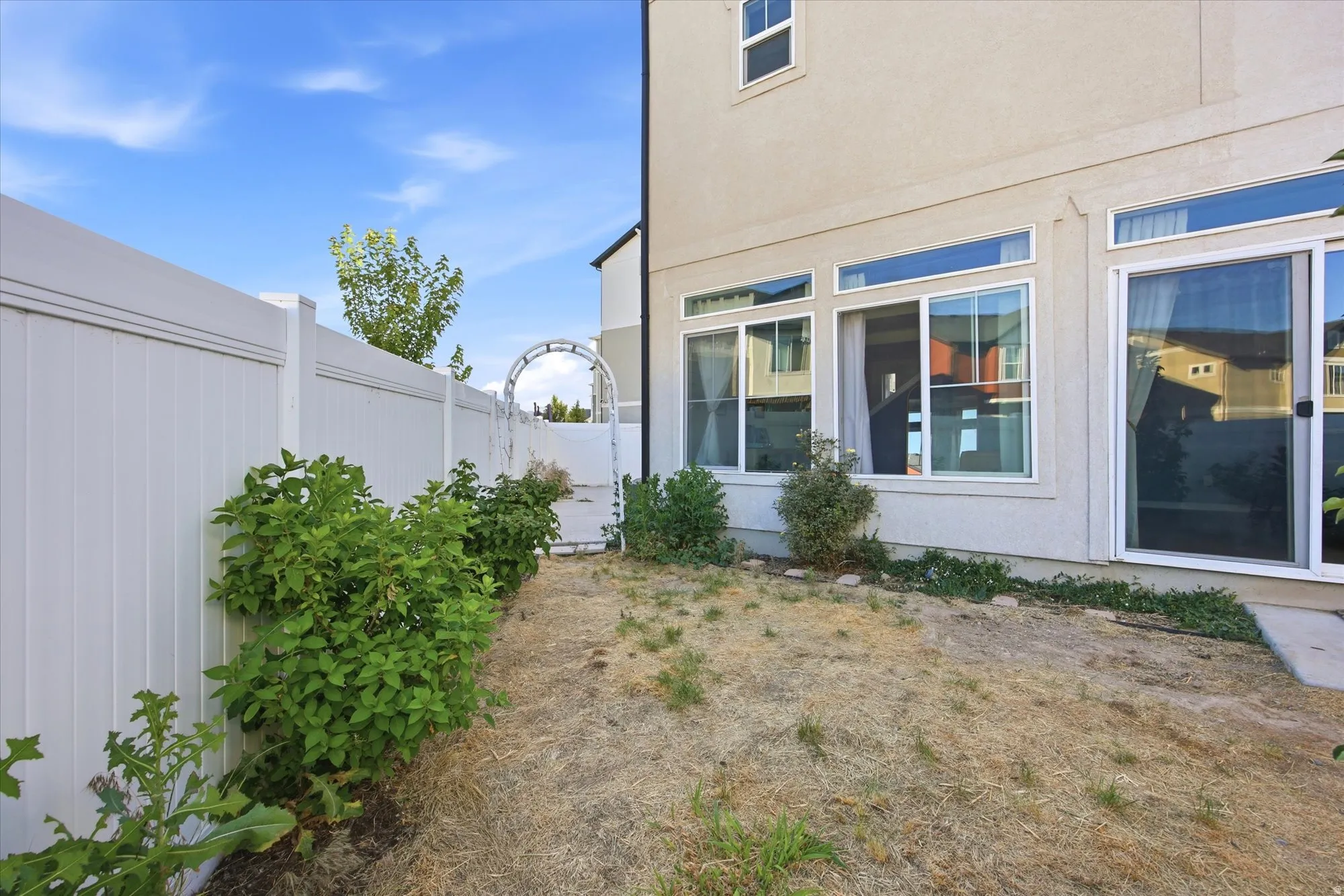 Enclosed backyard featuring a white privacy fence, mature perimeter shrubs, and a decorative garden archway