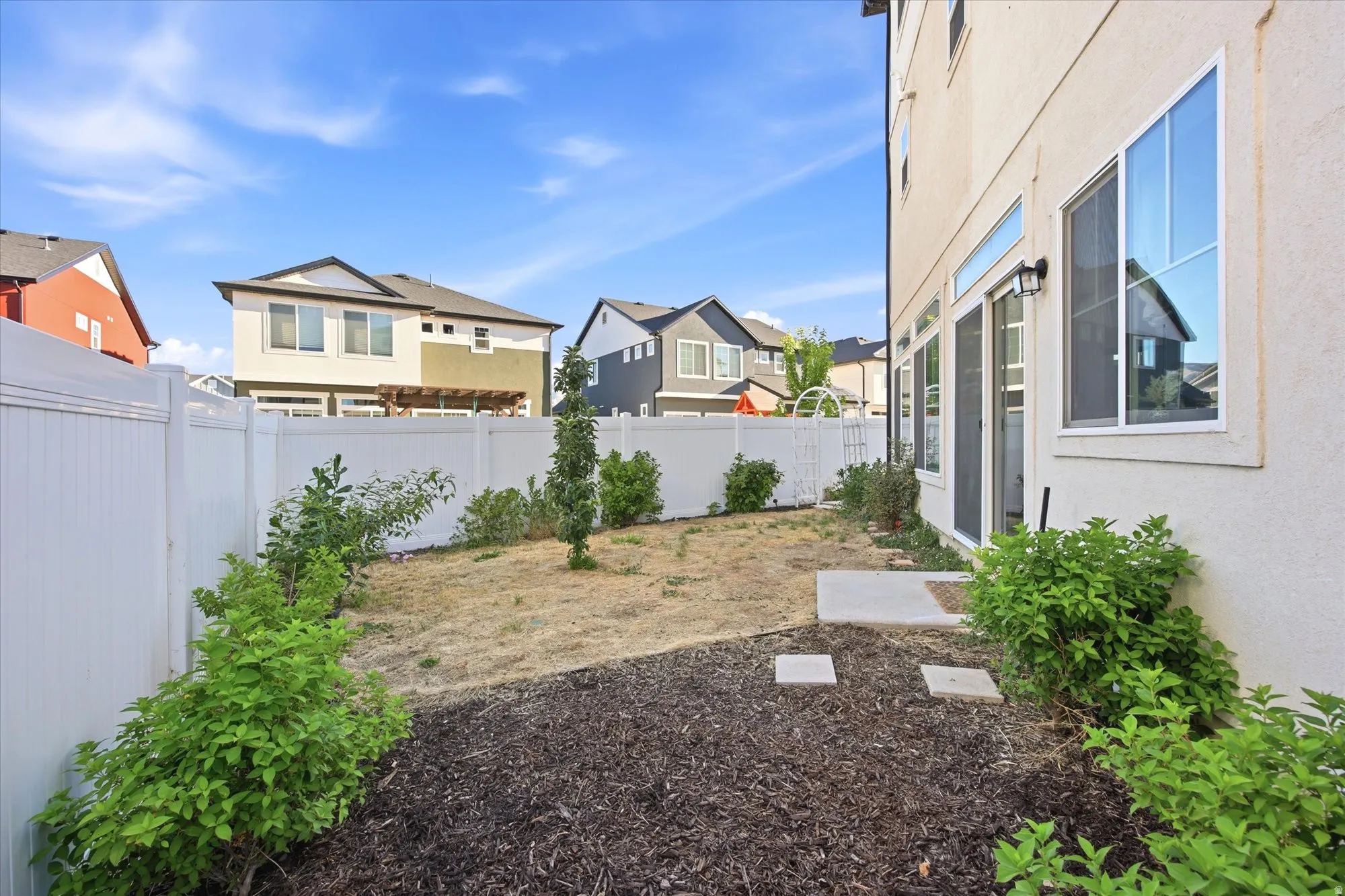 Private backyard featuring a white vinyl fence, established shrubbery, and a concrete patio