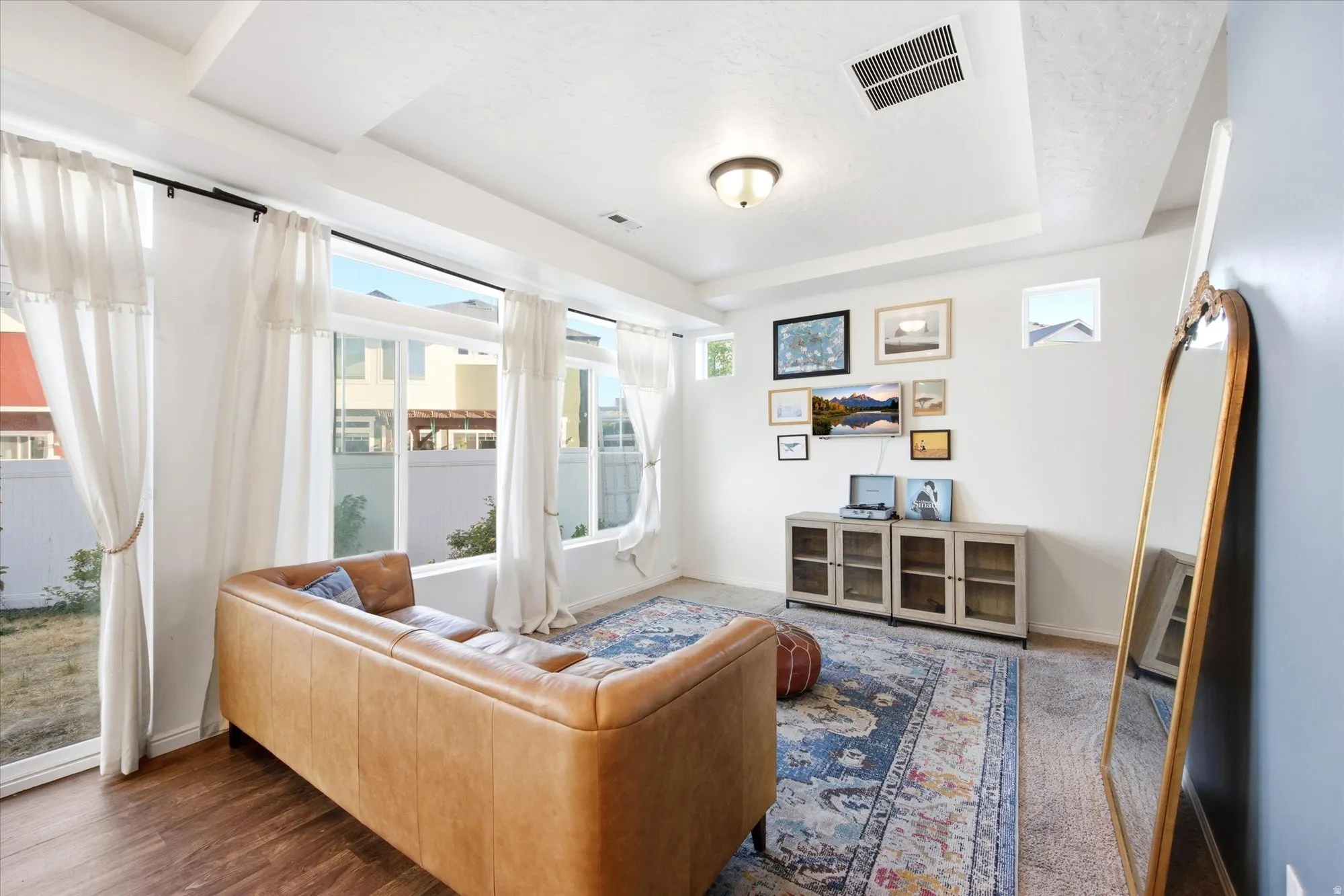 Living area featuring expansive windows, wood-finish flooring, a tray ceiling, and a built-in wall cabinet with glass doors