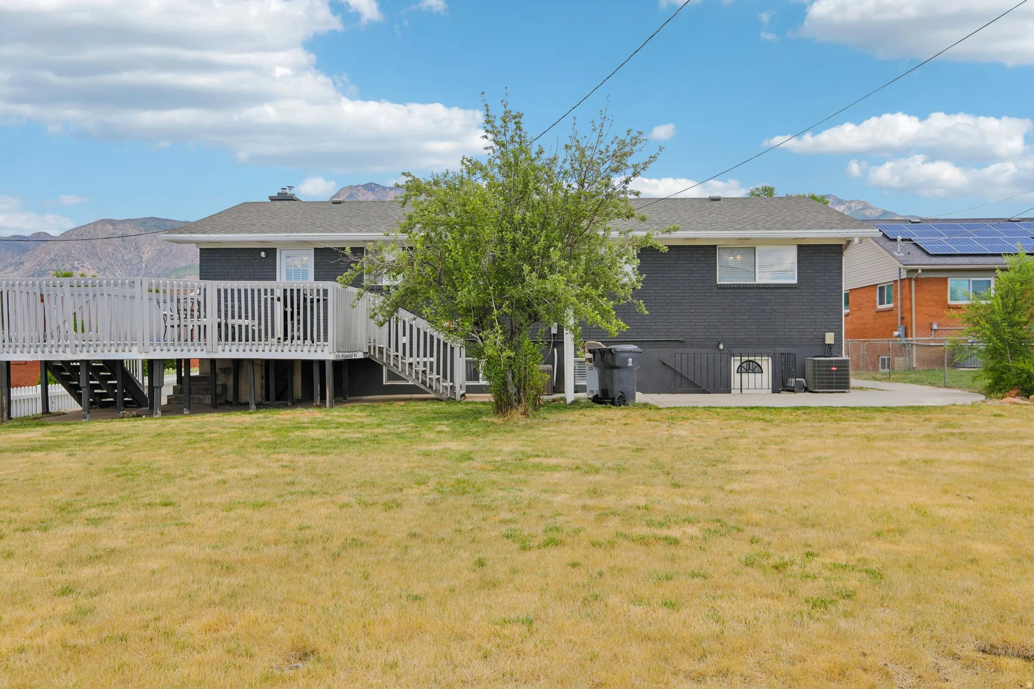 Expansive rear yard featuring a large elevated deck with white railing, a mature tree, and a concrete patio
