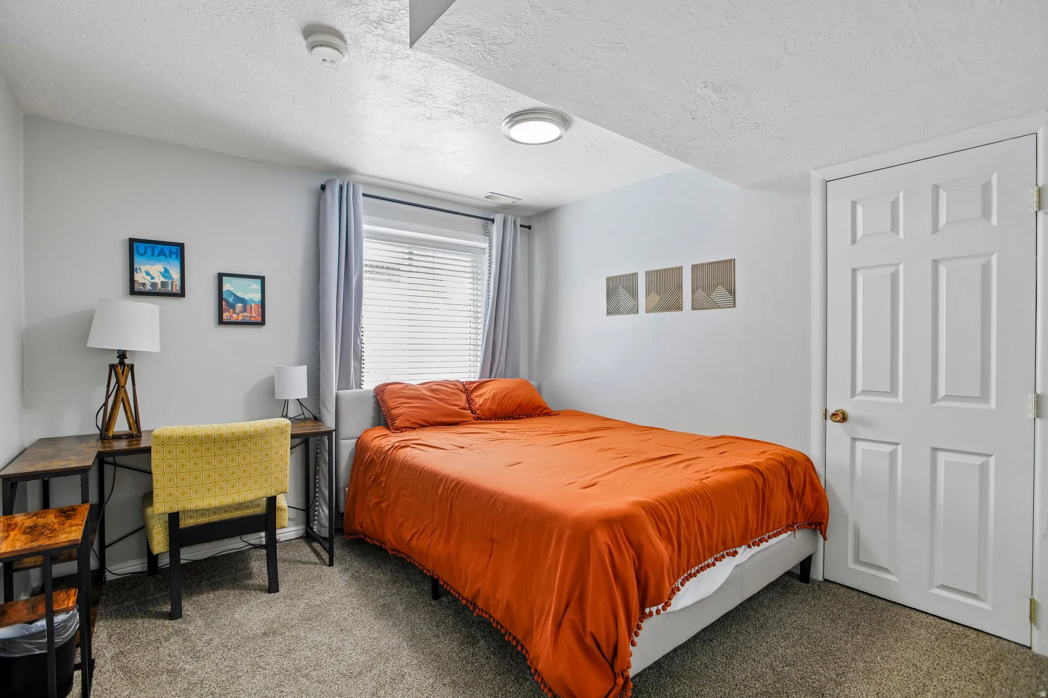 Carpeted bedroom featuring a white paneled door, a single window with blinds, and light gray walls