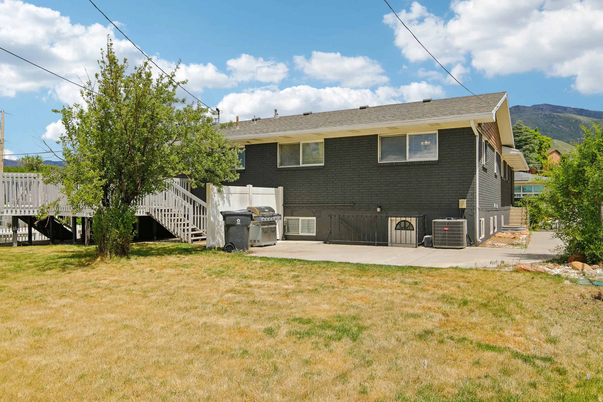Expansive backyard featuring a concrete patio, a multi-level wood deck with white railings, and mature trees
