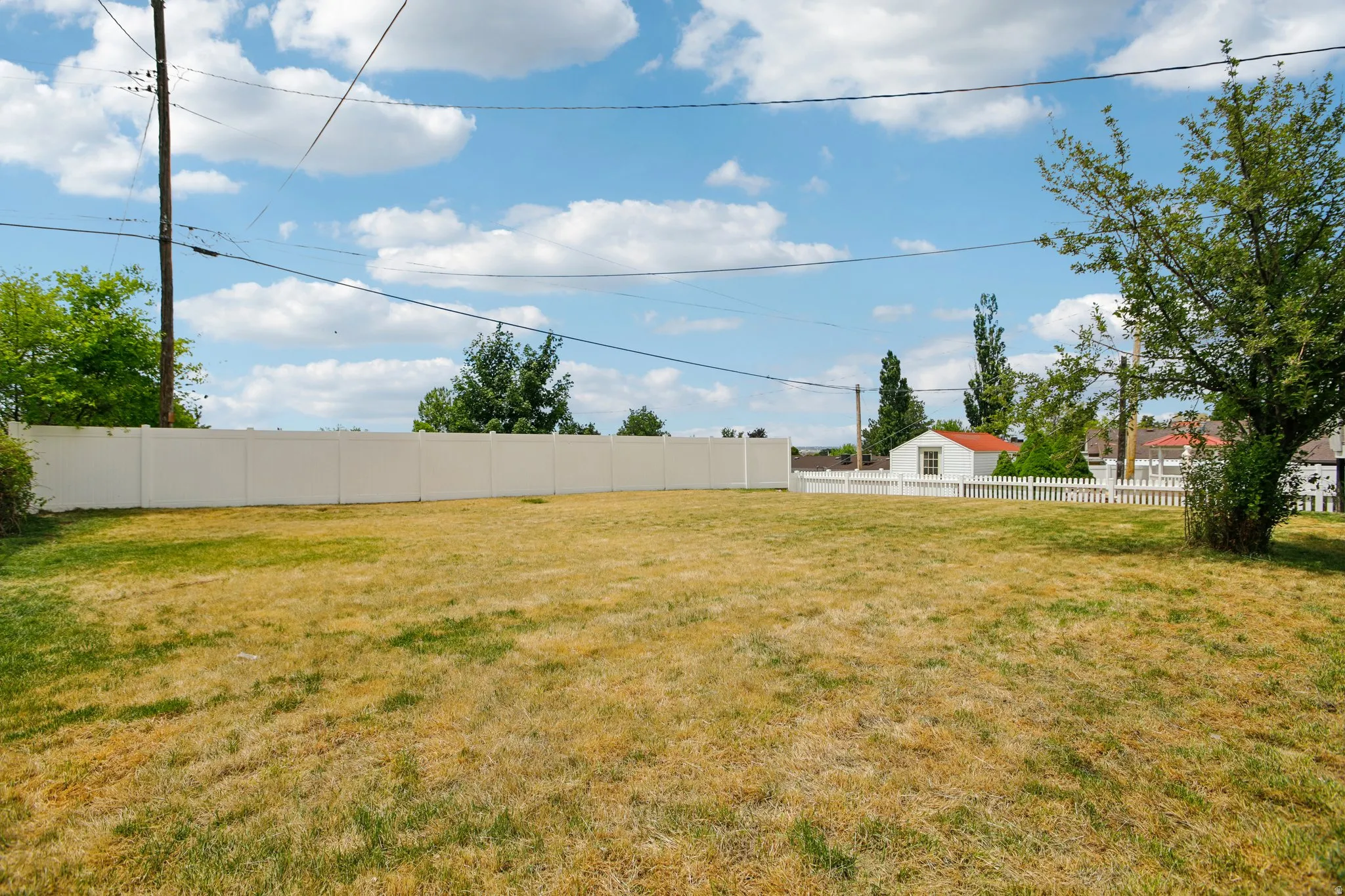 Expansive outdoor space featuring a large lawn area and a substantial white privacy fence