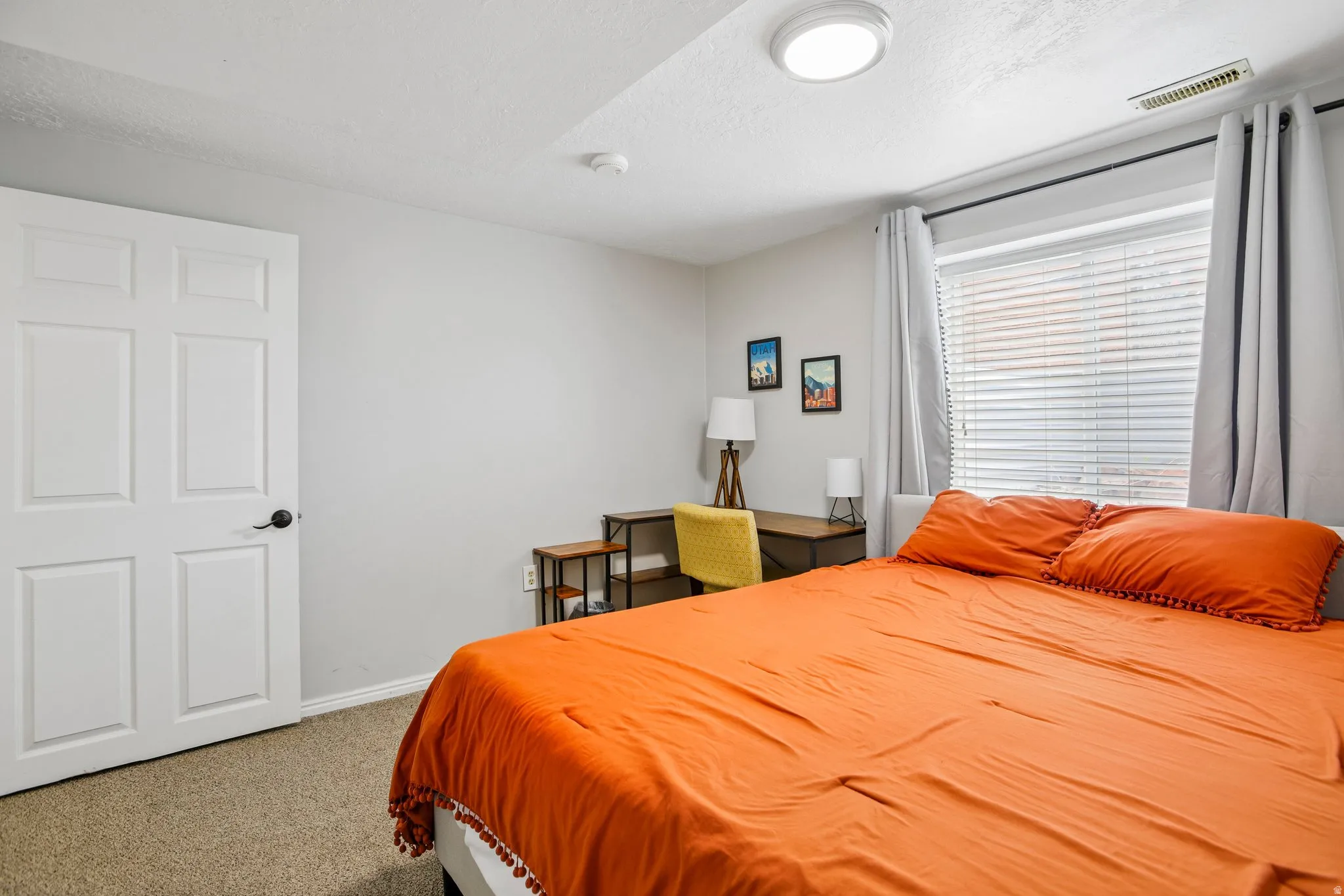 Bedroom featuring carpet flooring, a window with blinds and gray curtains, a flush-mount ceiling light, and light gray painted walls