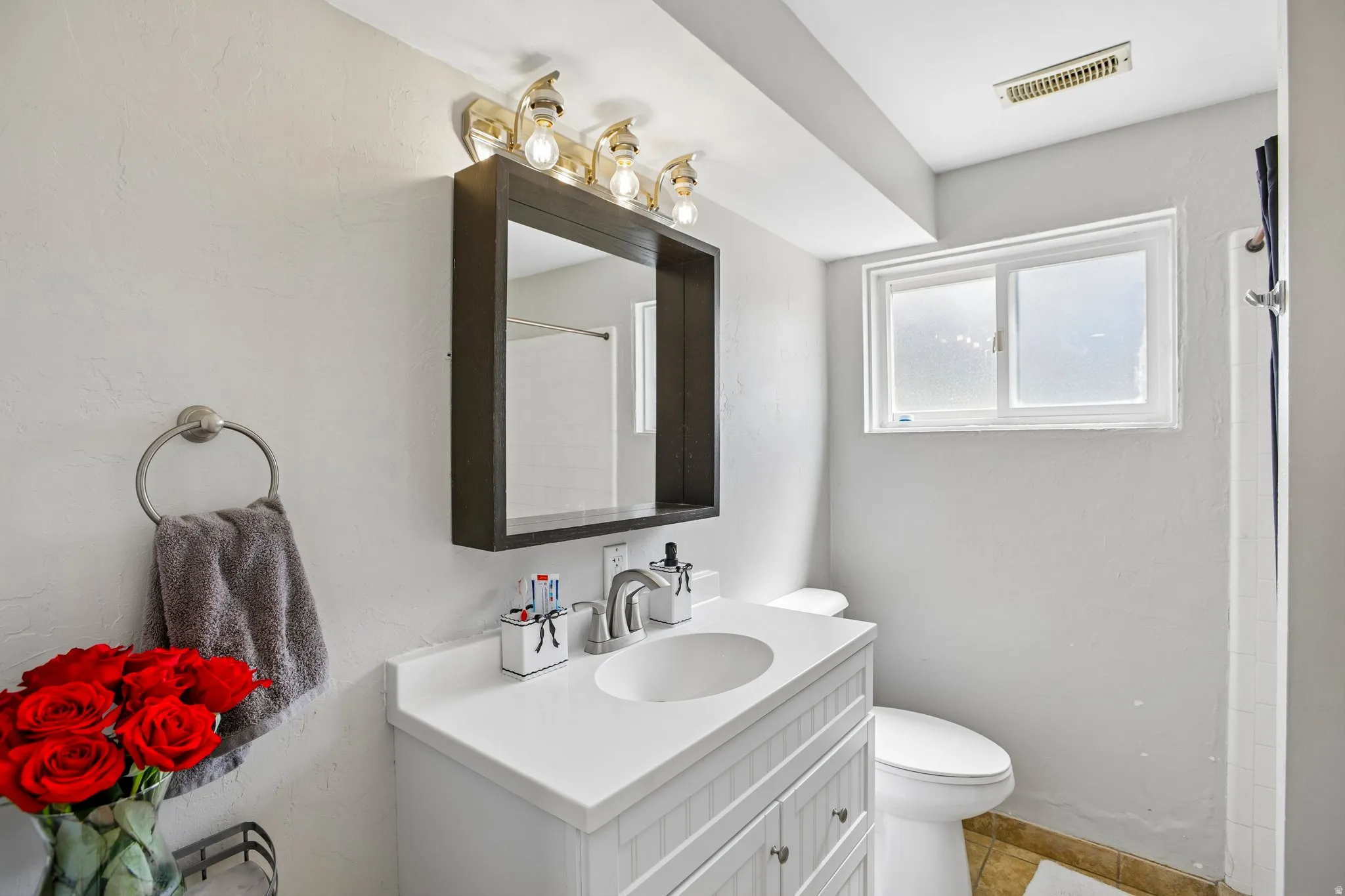 Bathroom featuring a white vanity with an integrated sink and brushed nickel faucet, a medicine cabinet with a dark frame, and multi-bulb vanity lighting