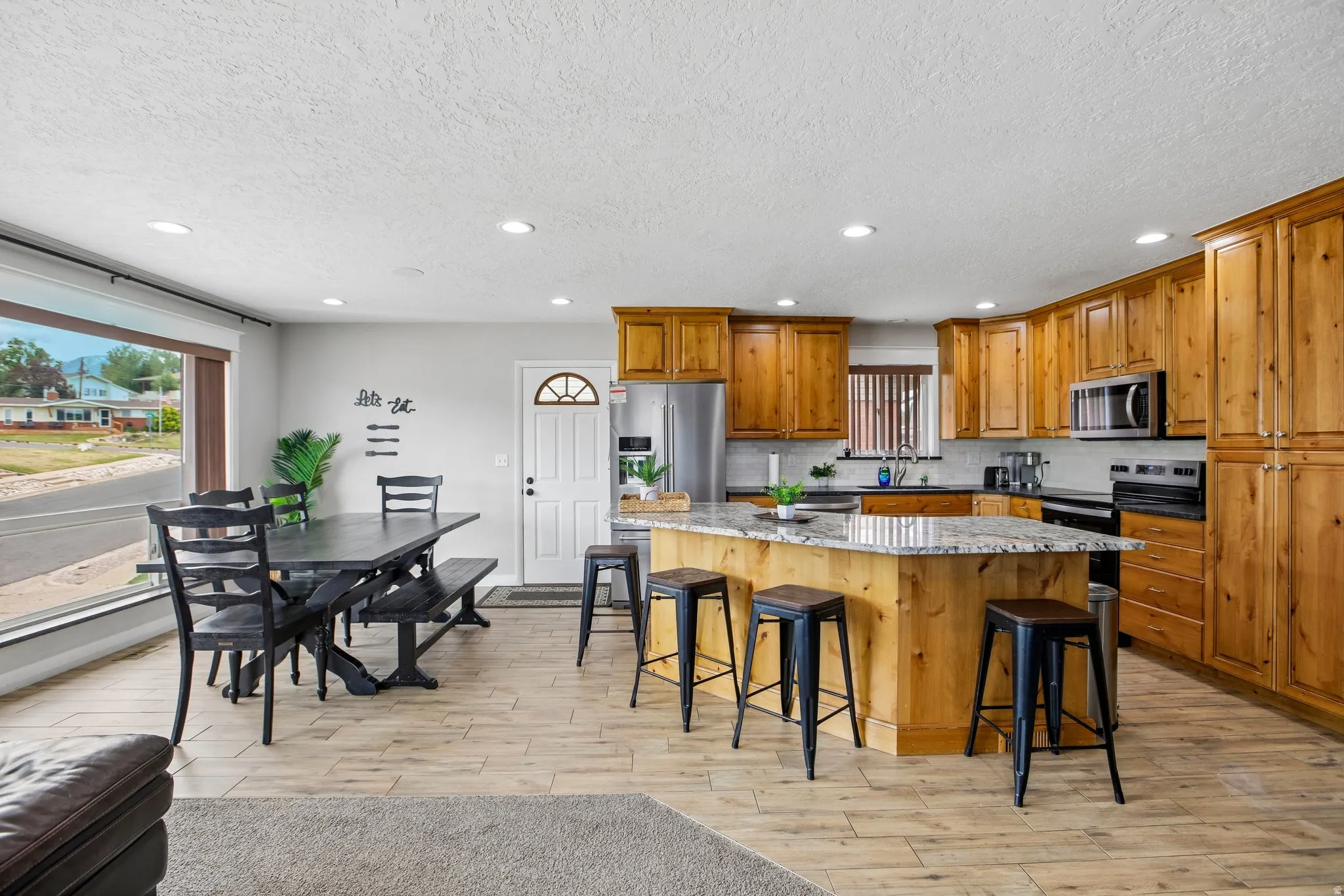 Open-concept kitchen and dining area featuring warm wood cabinetry, a central island with bar seating, and stone-finish countertops