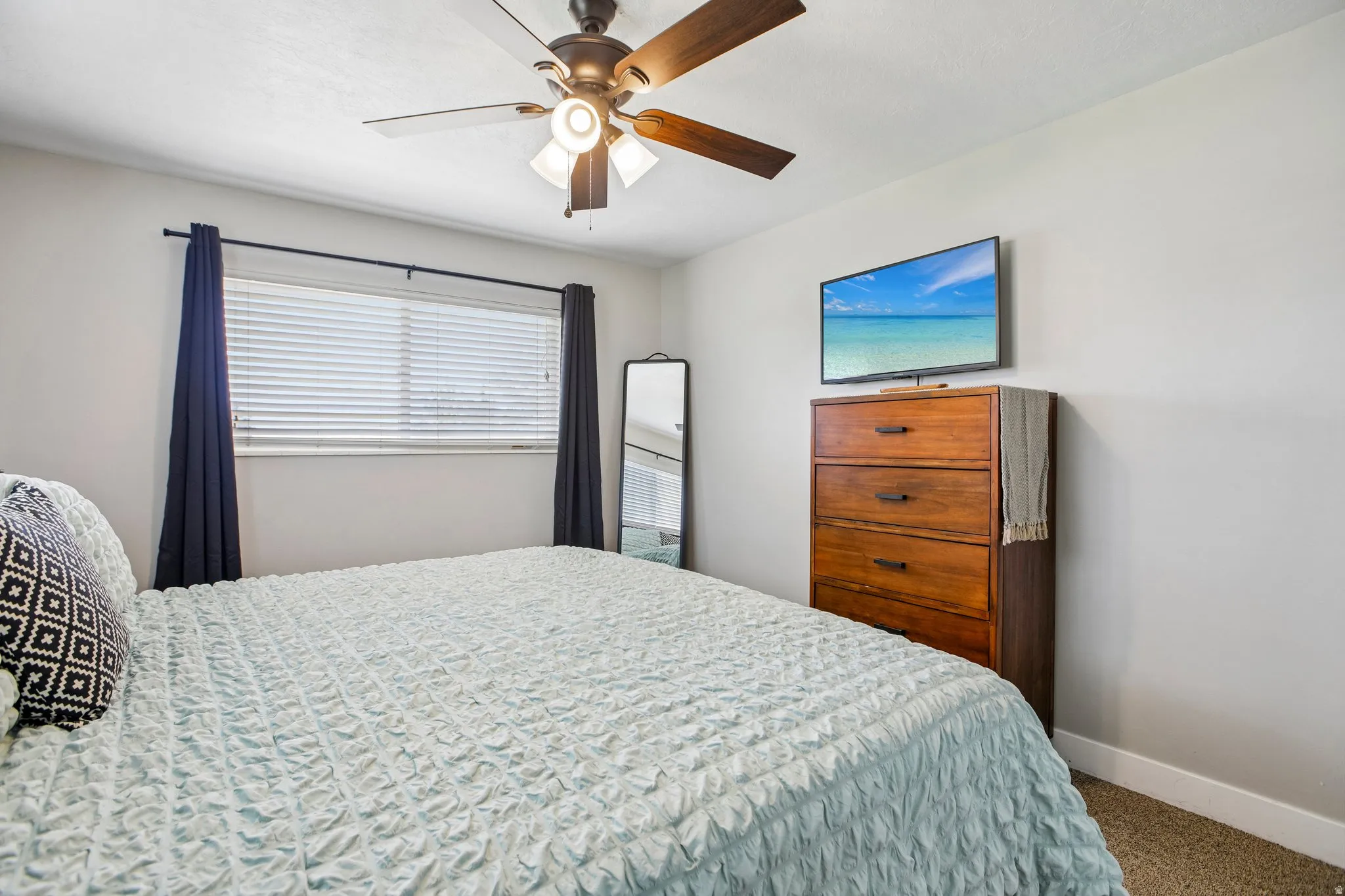 Neutral-toned interior with a ceiling fan featuring integrated lighting, a window with horizontal blinds, and carpeted flooring