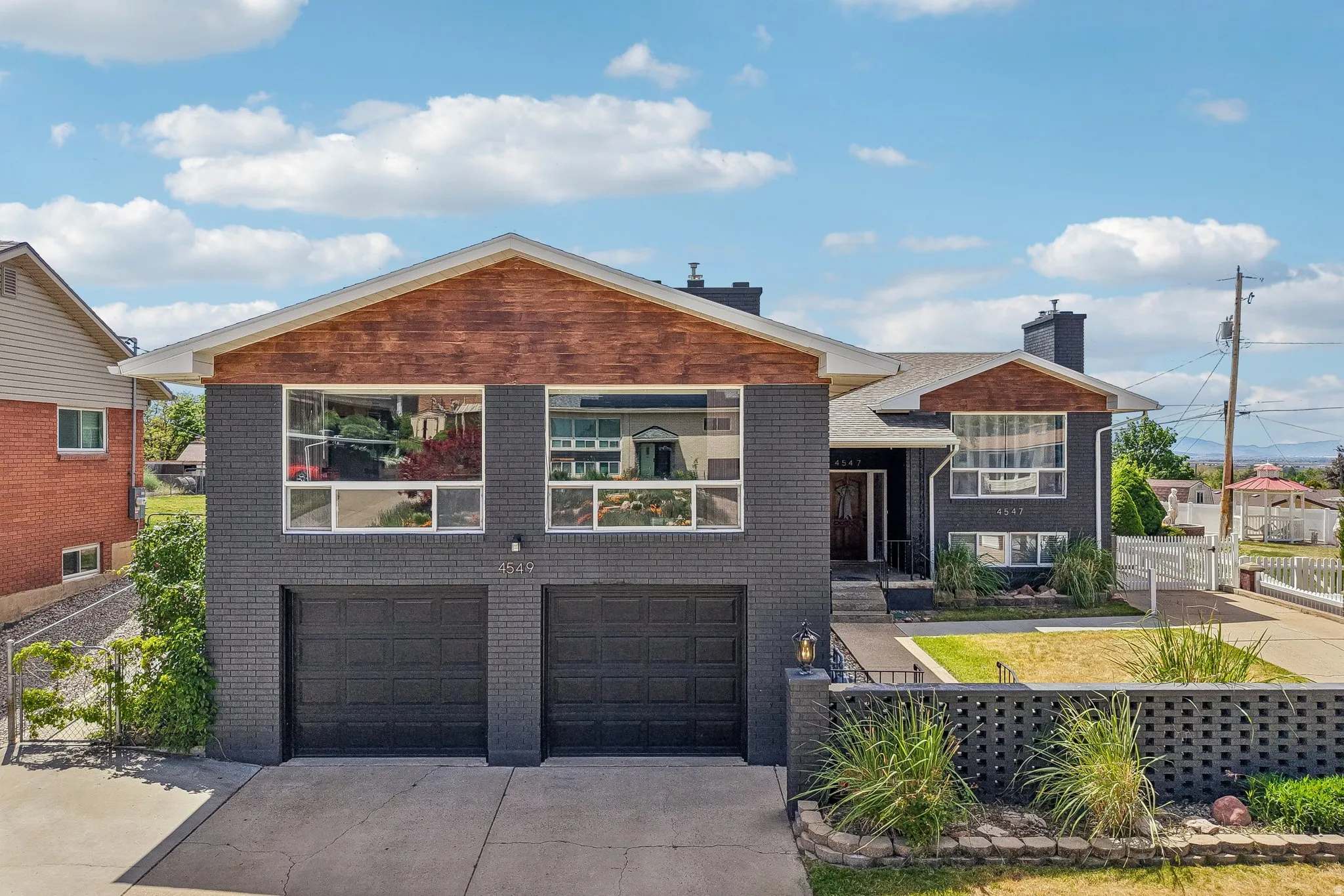 Split-level residence featuring a dark brick exterior with wood-finish gables and a two-car garage