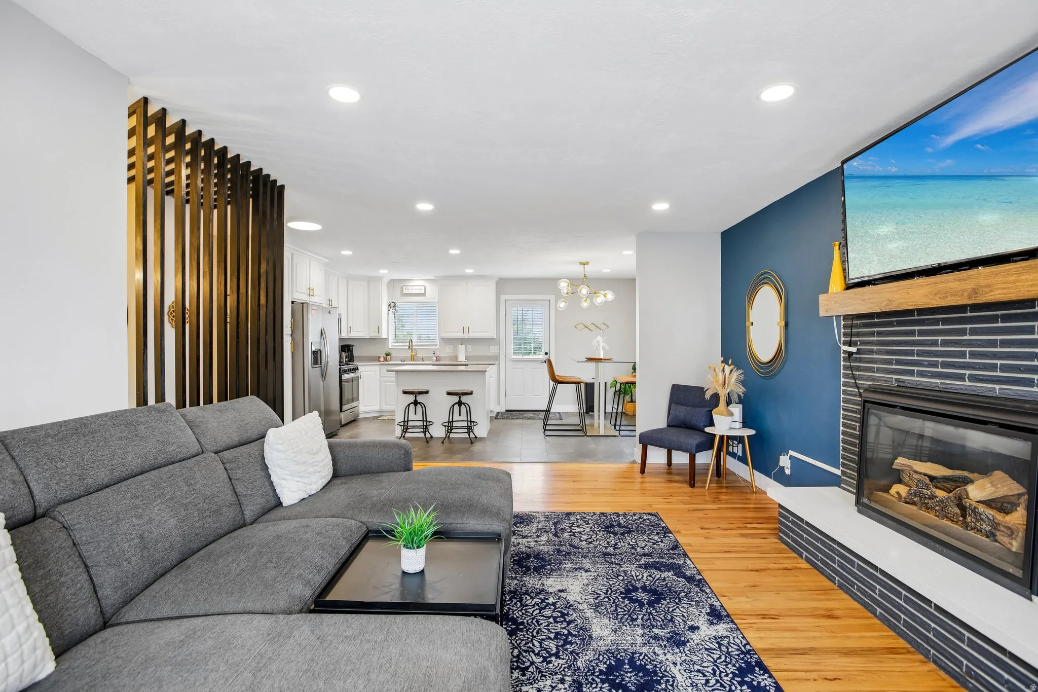 Open-concept living area featuring wood-finish flooring, a contemporary fireplace with a dark tile surround, and a decorative wood slat wall