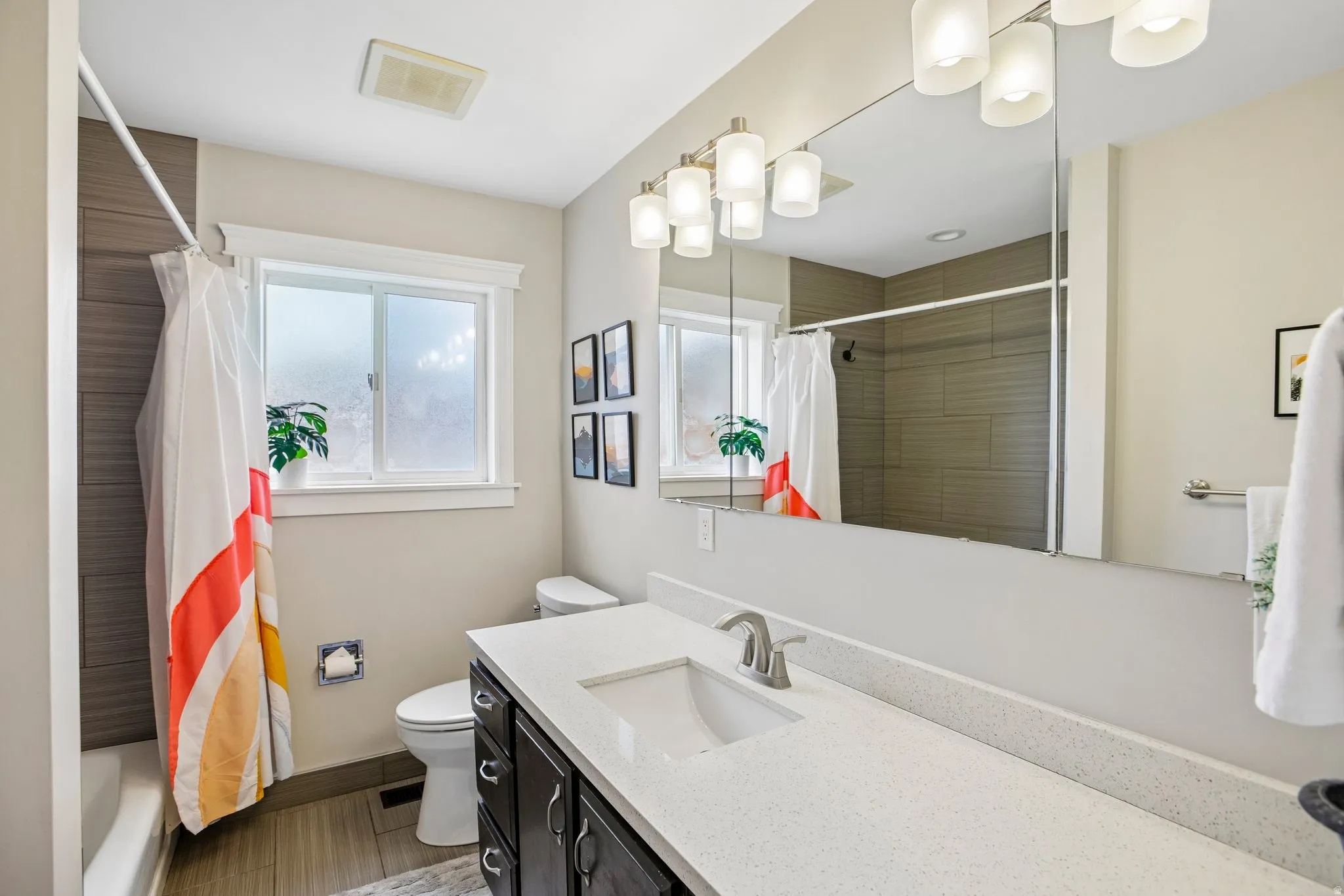 Bathroom featuring a spacious vanity with an integrated sink, a large wall-mounted mirror, and contemporary lighting fixtures
