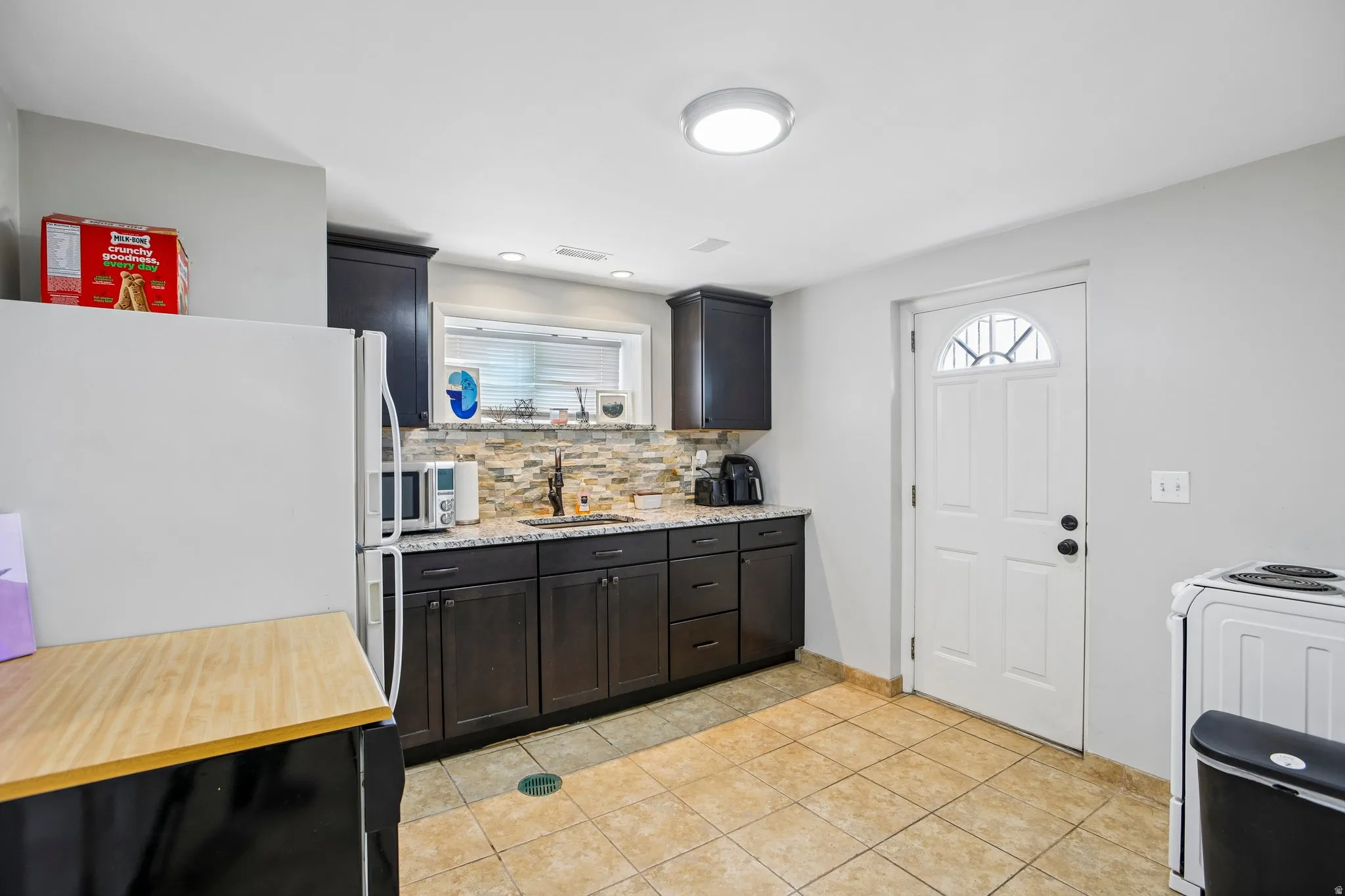 Kitchen area featuring dark wood-finish cabinetry, granite-style countertops, and a stone tile backsplash