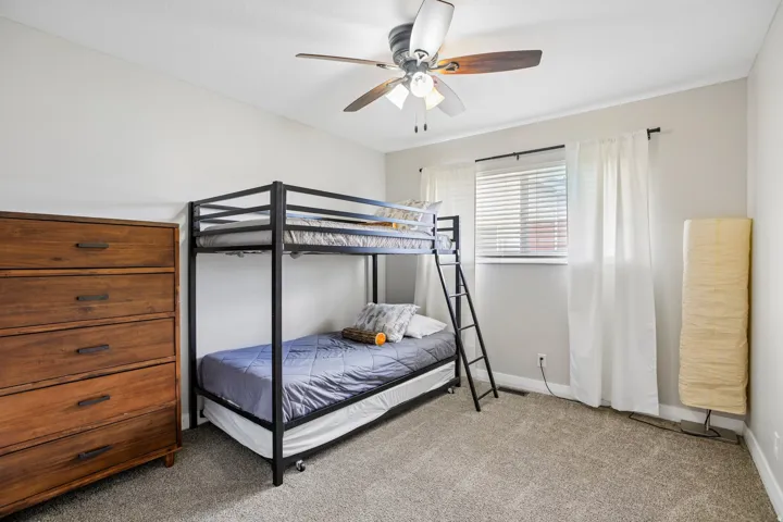 Carpeted room featuring a ceiling fan with light fixture, a window with blinds and drapes, and neutral wall paint
