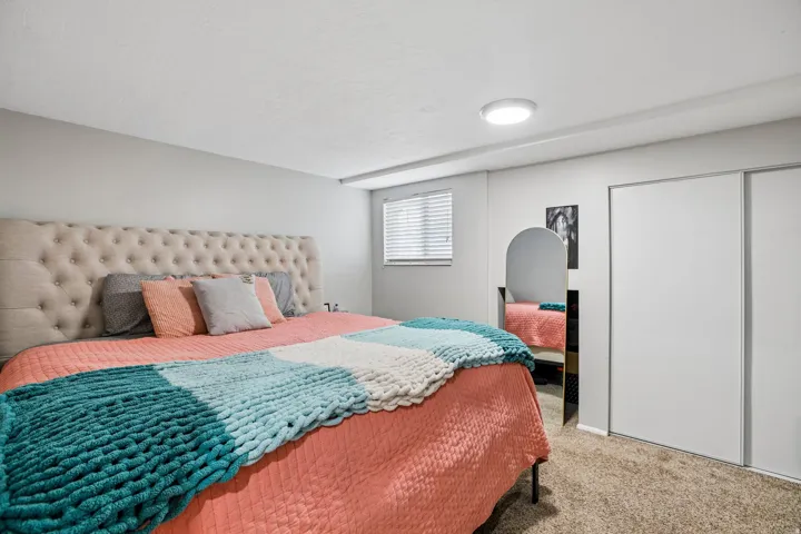 Bedroom featuring a button-tufted upholstered headboard, a window with horizontal blinds, a flush-mount ceiling light fixture, and sliding closet doors