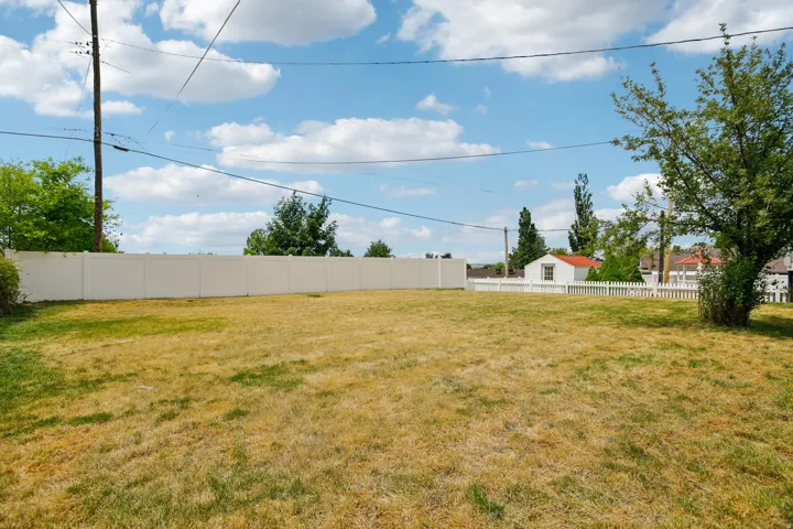 Expansive outdoor space featuring a large lawn area and a substantial white privacy fence