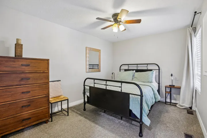 Spacious room featuring neutral wall tones, textured carpeting, a ceiling fan with integrated lighting, and a window with blinds