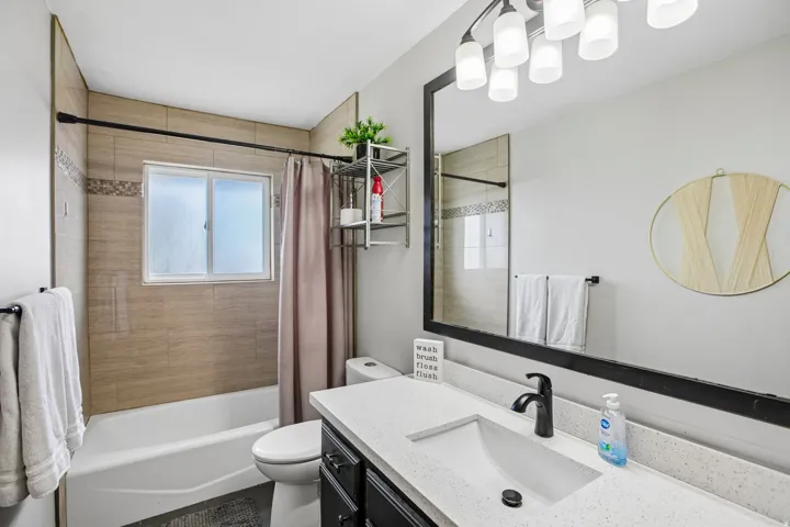 Bathroom featuring a tub/shower combination with subway tile surround and decorative accent band, a single window, and a dark-finish vanity with a light-tone countertop and integrated sink