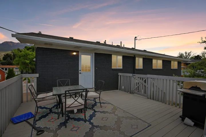 Spacious outdoor deck featuring a perimeter railing, direct exterior access, a dark-toned brick facade, multiple windows, and mountain scenery
