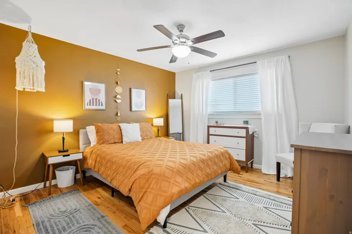 Bedroom featuring wood-finish flooring, a ceiling fan with integrated lighting, and a window with blinds and curtain rods