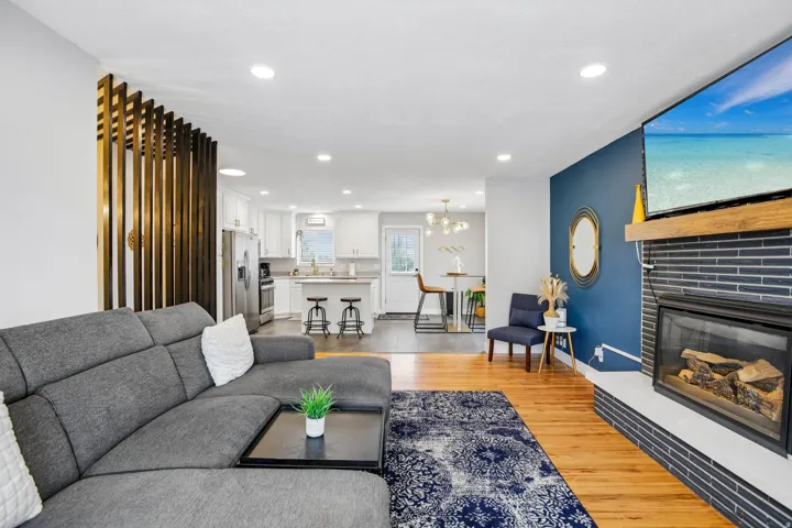 Open-concept living area featuring wood-finish flooring, a contemporary fireplace with a dark tile surround, and a decorative wood slat wall