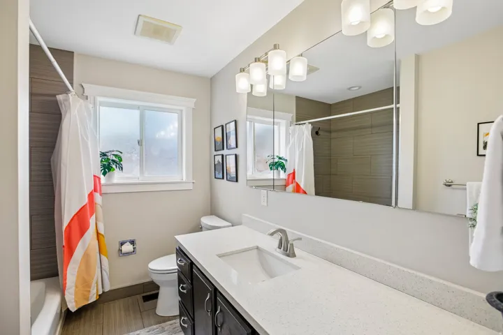 Bathroom featuring a spacious vanity with an integrated sink, a large wall-mounted mirror, and contemporary lighting fixtures