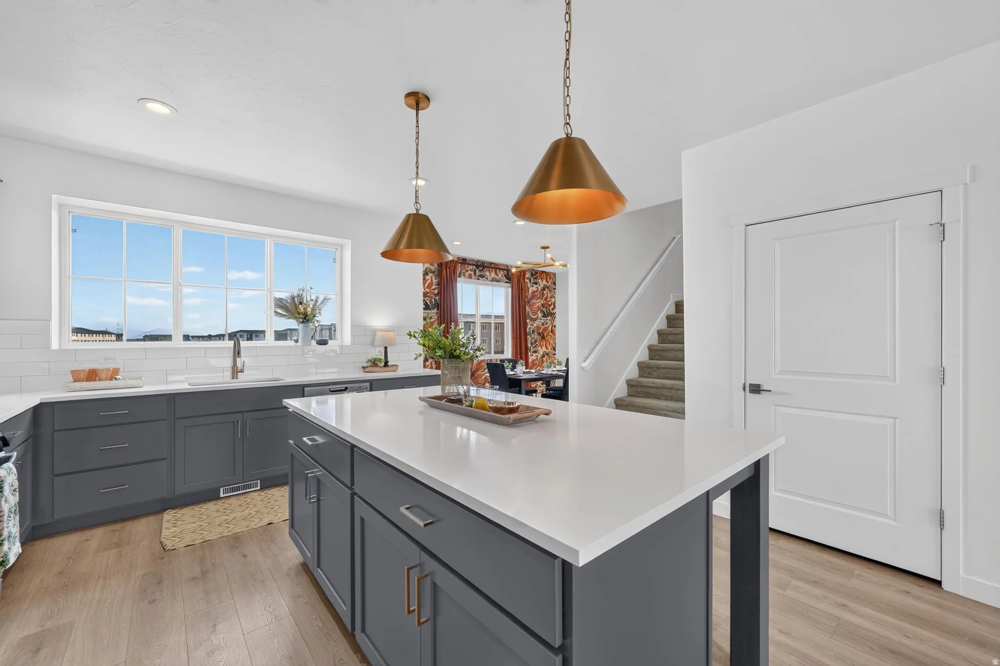 Modern kitchen featuring an expansive center island with a white countertop, two brass pendant lights, and wood-finish flooring