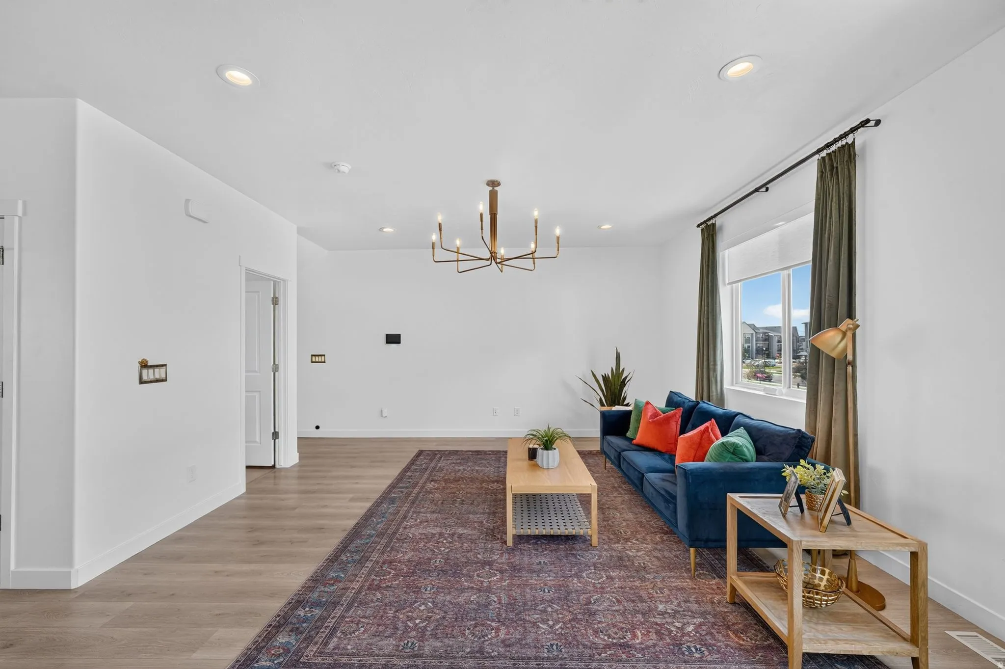 Spacious living area featuring light wood-finish flooring, recessed lighting, and a modern chandelier