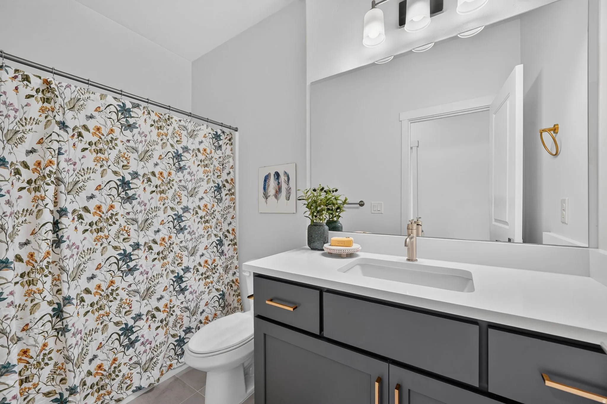 Bathroom featuring a dark gray vanity with gold-tone hardware, a white countertop with an integrated sink, and a large mirror