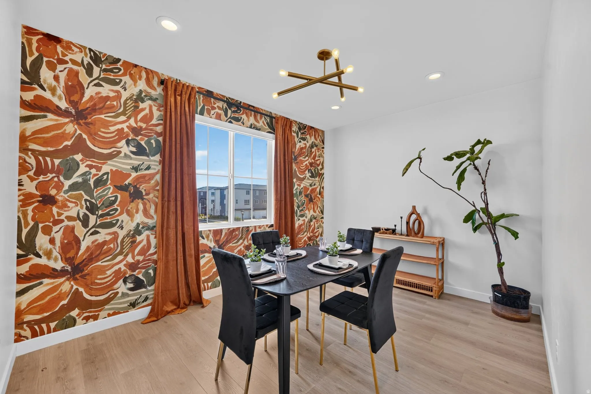 Dining area featuring a prominent accent wall with a floral pattern, wood-finish flooring, and a modern linear chandelier