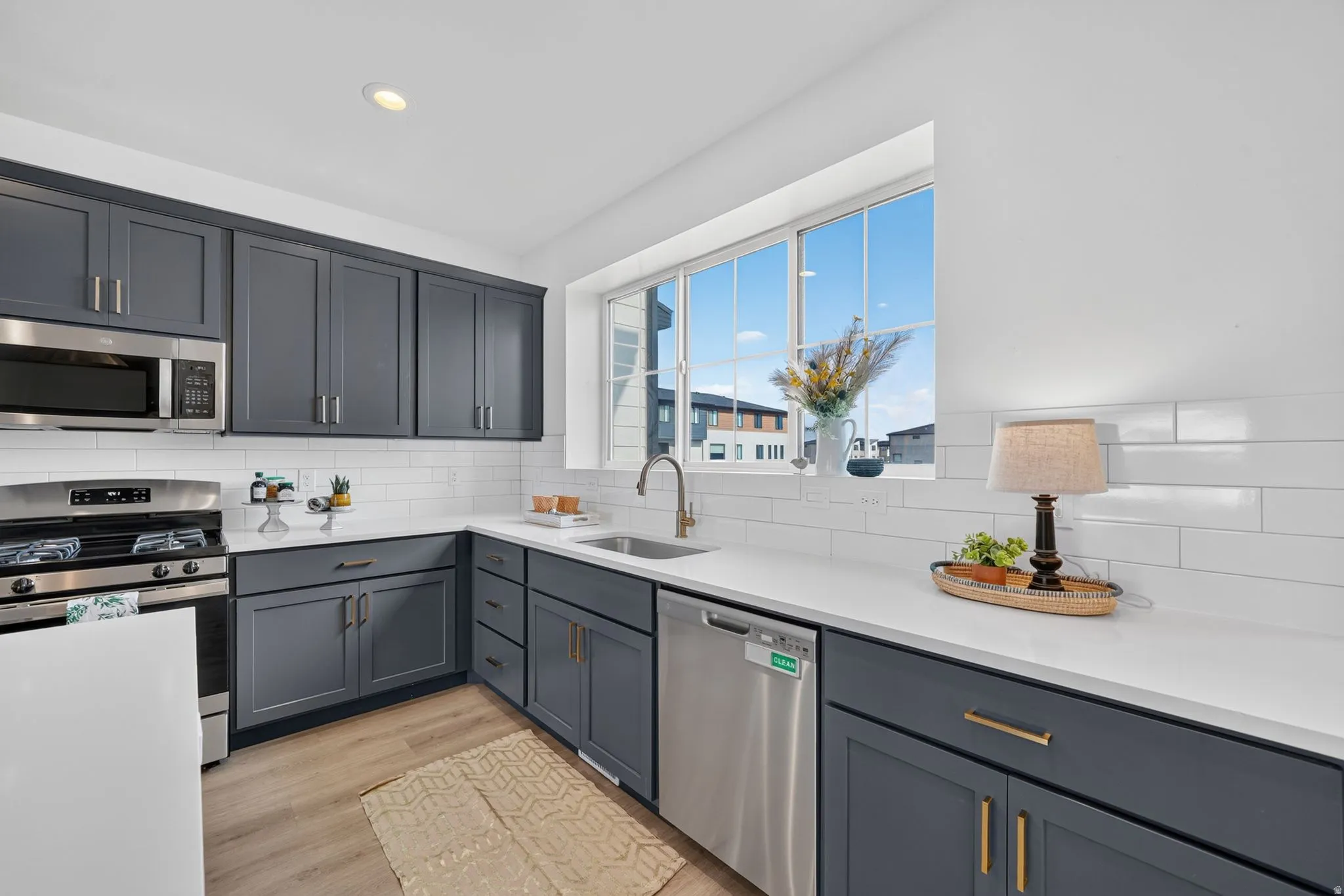 Contemporary kitchen featuring dark gray cabinetry, stainless steel appliances, white subway tile backsplash, and light wood-finish flooring