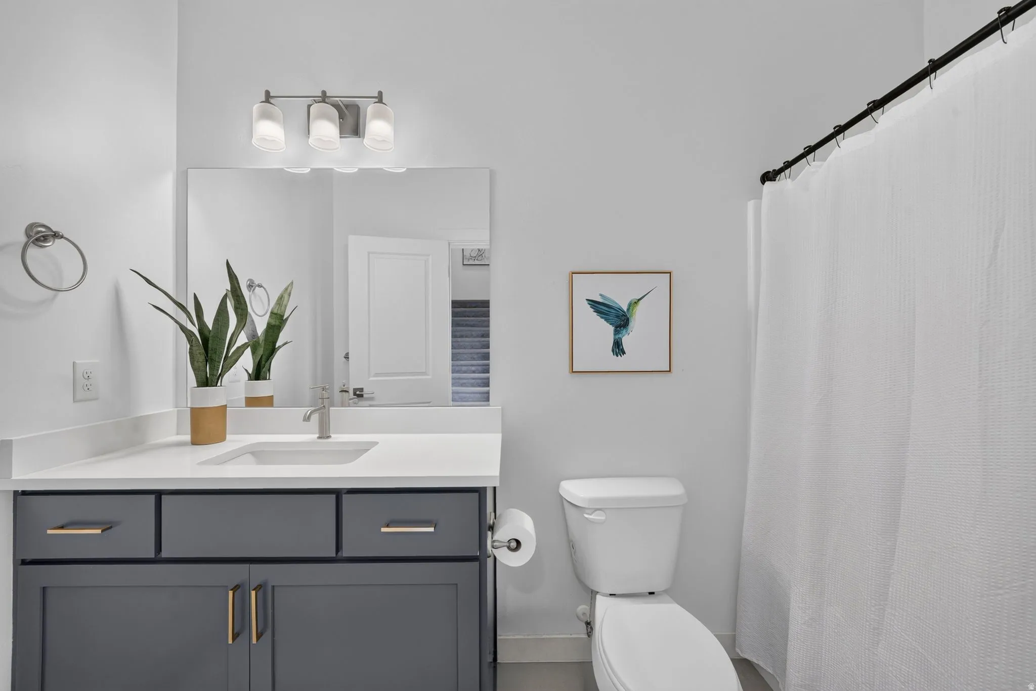 Bathroom featuring a modern vanity with dark gray cabinetry, gold-tone hardware, and a white countertop with an integrated sink