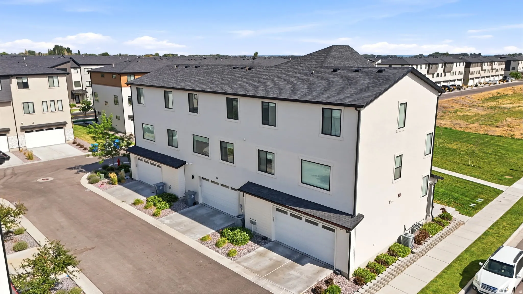 Contemporary multi-story residence featuring a light-colored stucco exterior, black-framed windows, and a dark-shingled roof