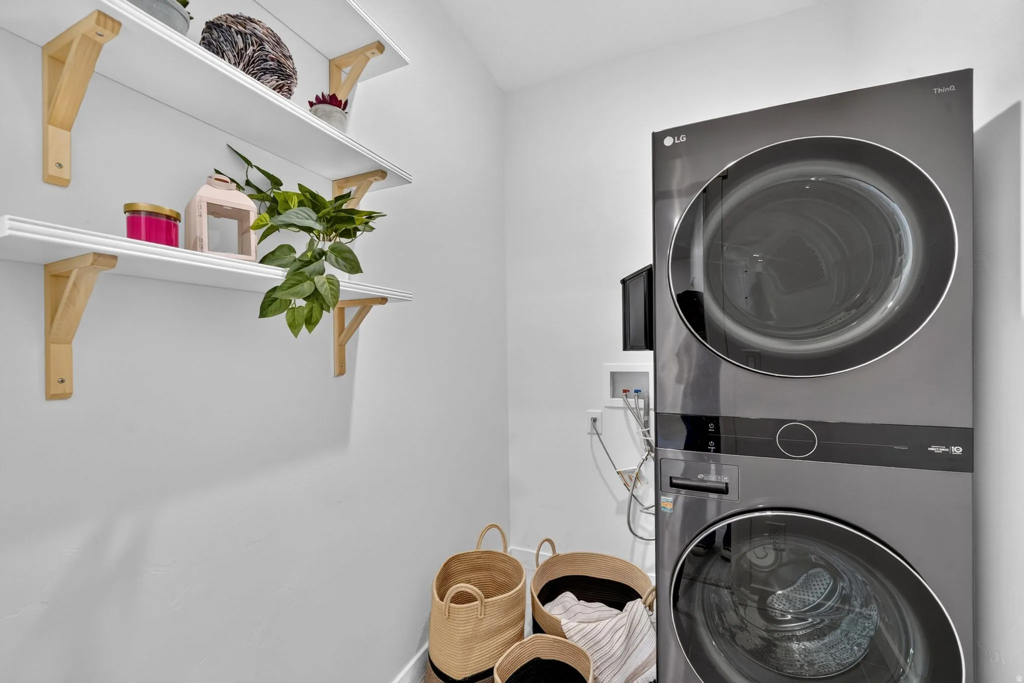 Dedicated laundry area featuring a stacked washer and dryer, white walls, and built-in floating shelves with natural wood brackets